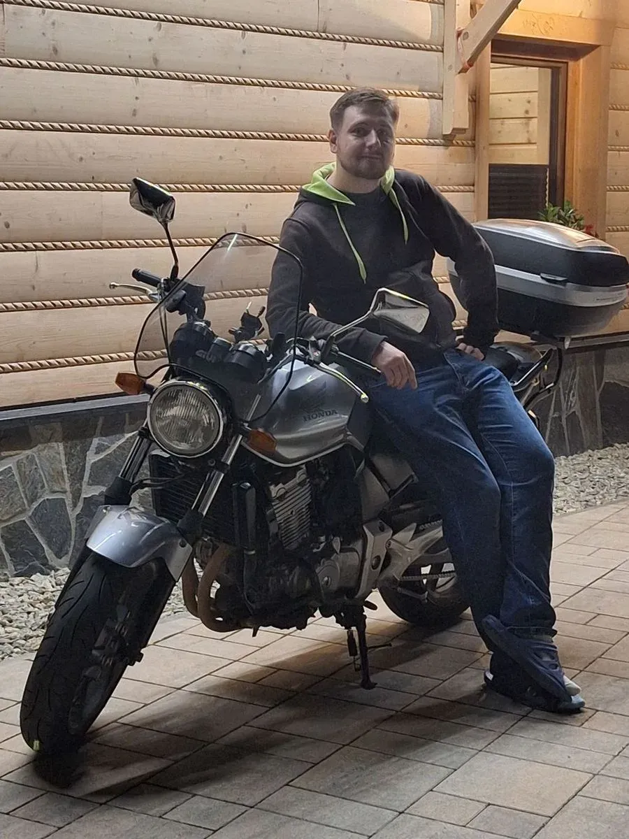 Andrzej Chmiel sitting on a silver Honda motorcycle outside a wooden house